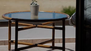 A glass-top table with a potted plant, set on a balcony with a view of the sea and greenery.