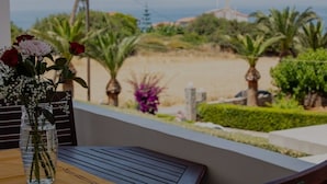 A balcony with a view of a beach, palm trees, and a clear sky.