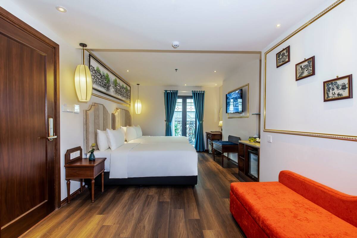 A hotel room with a large bed, a wooden floor, a desk with a chair, a TV, and framed pictures on the wall.
