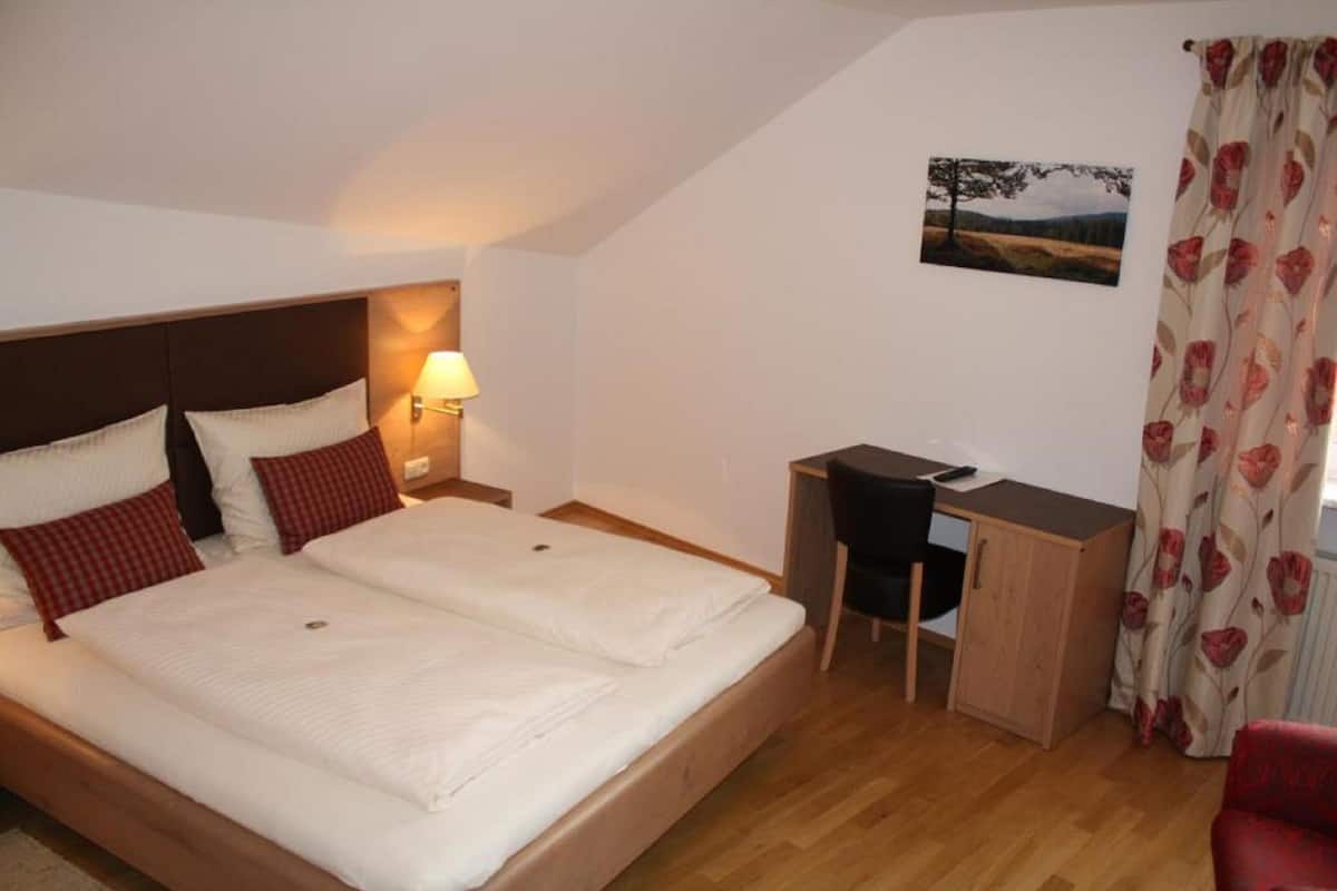 A bedroom with a bed, desk, chair, and a wall-mounted lamp.