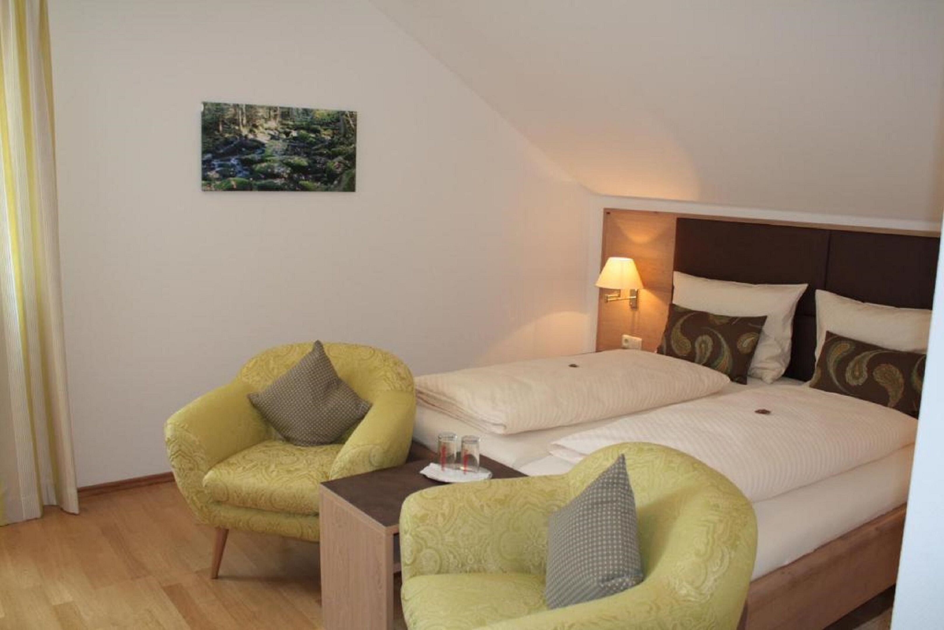 A hotel room with a bed, two armchairs, a small table, and a wall-mounted lamp.