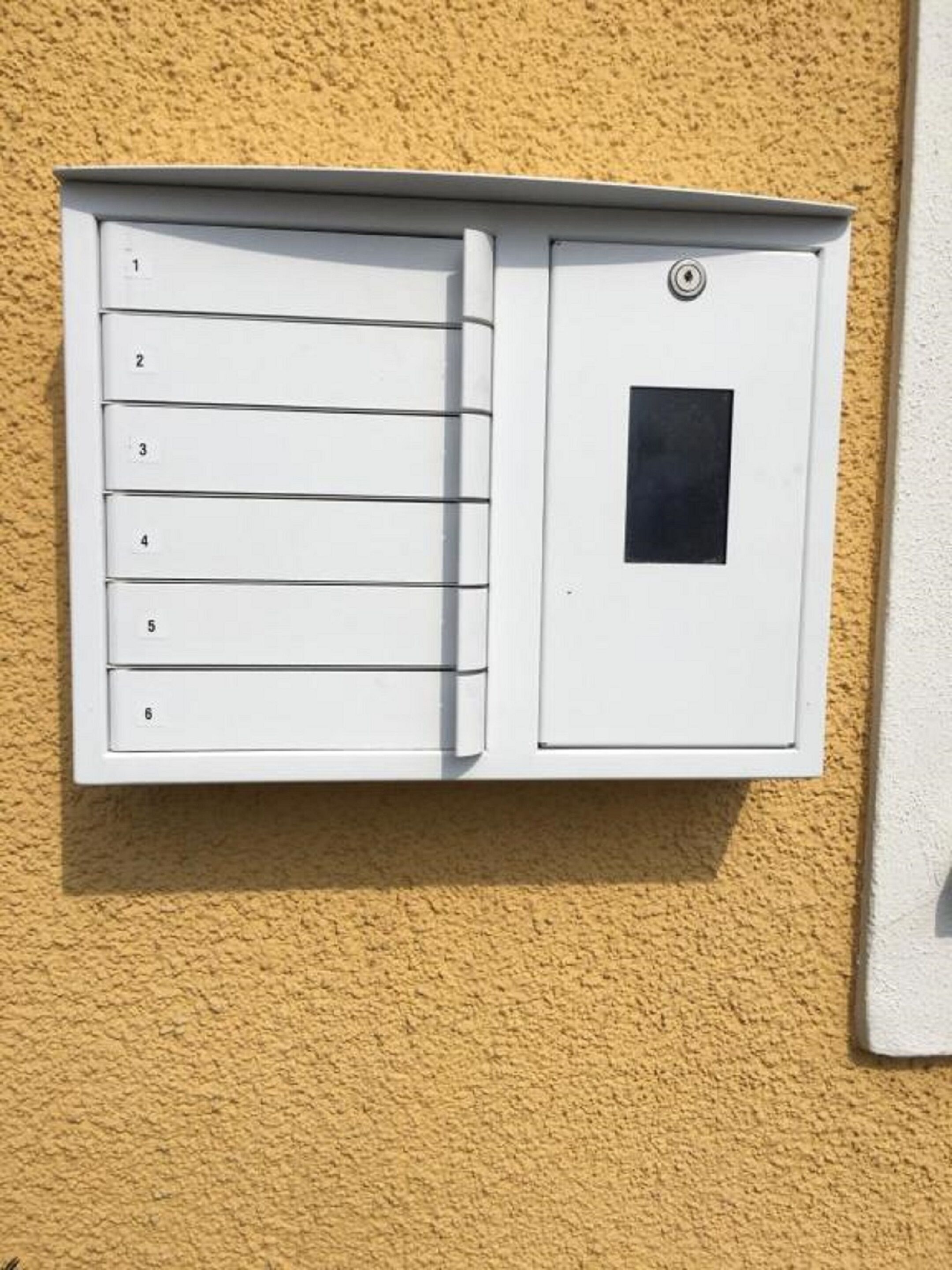 A white utility box with numbered slots, likely for mail or deliveries, mounted on a textured yellow wall.