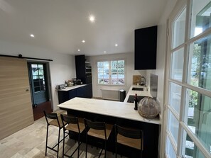 A modern kitchen with a large island, bar stools, and a view of the outdoors through a window. - Villa Arcachon/abatilles Piscine / Lisière Foret (Arcachon)