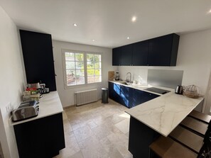A modern kitchen with dark cabinets, a white countertop, a window with a view, and a built-in stove. - Villa Arcachon/abatilles Piscine / Lisière Foret (Arcachon)