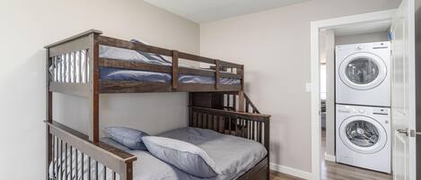 Ein Stockbett mit Holzbettrahmen und Schubladen, eine Waschmaschine und eine Tür zu einem anderen Raum.
