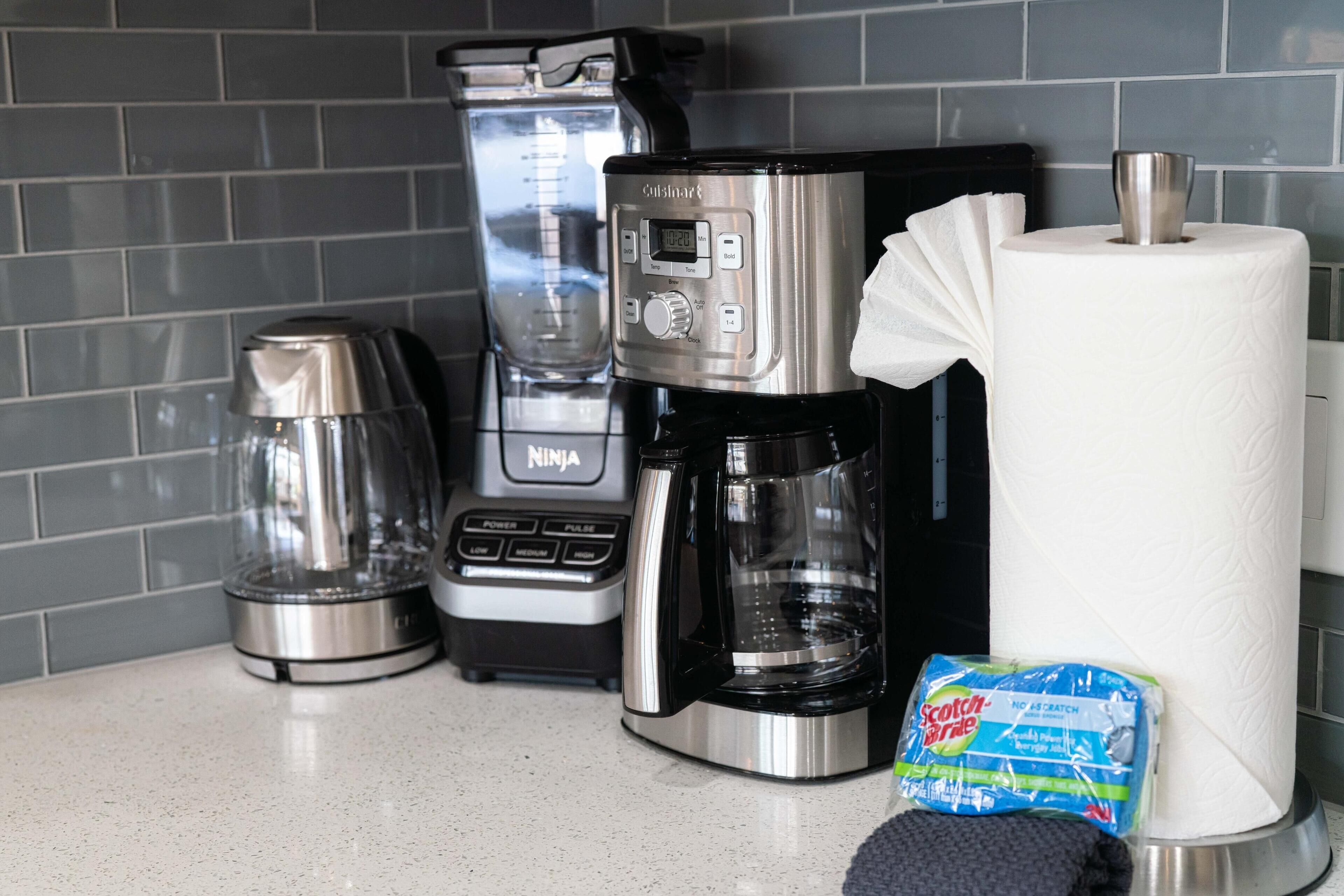 A kitchen counter with a coffee maker, a blender, and a package of Scotch Brite.