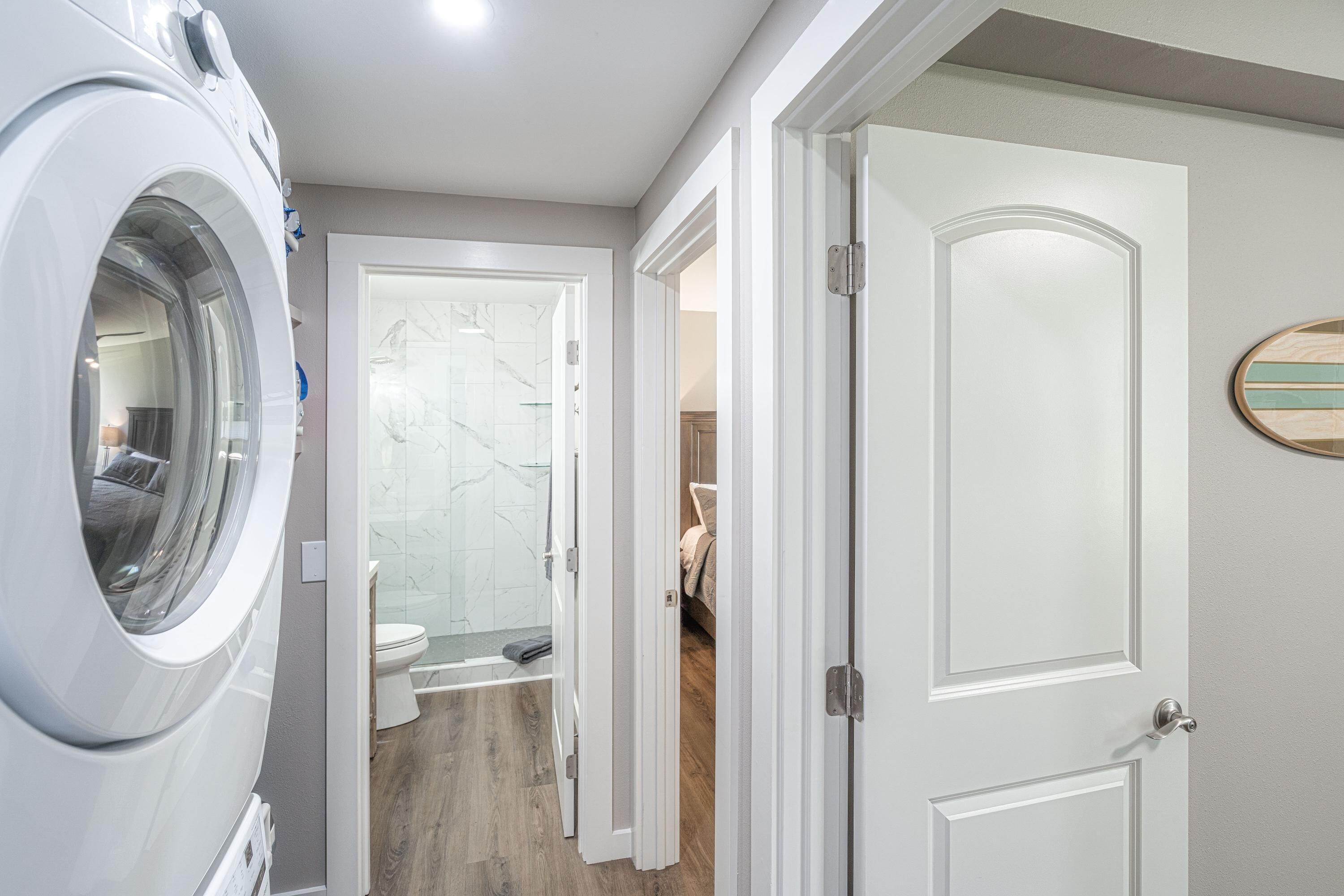 A laundry area with a washing machine, a glass shower enclosure, and a wooden floor.