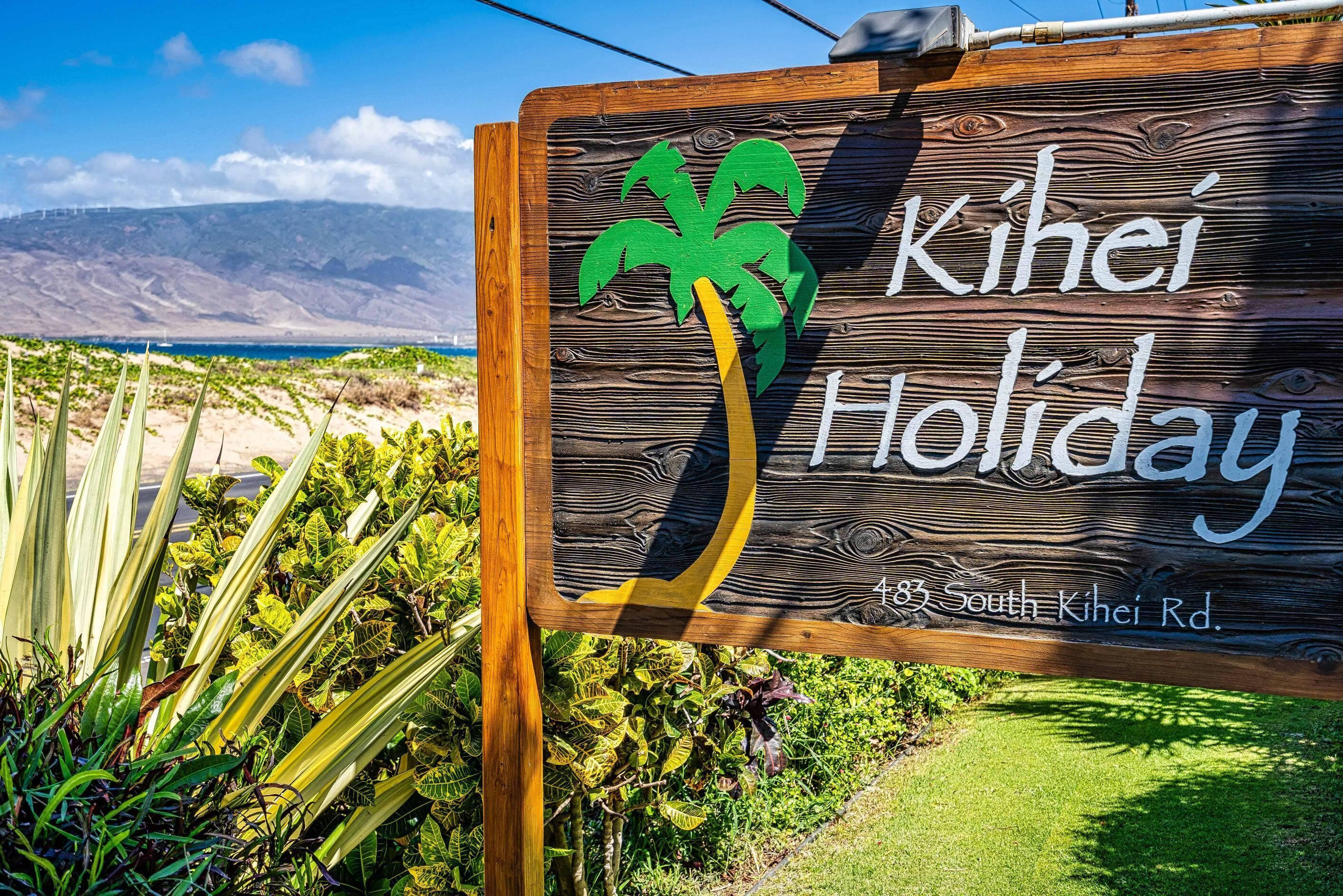 Un panneau en bois représentant un palmier et portant l’inscription « Kihei Holiday » et l’adresse « 483 South Kihei Rd. ».