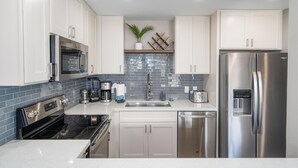 A modern kitchen with white cabinets, stainless steel appliances, a tiled backsplash, and a built-in oven. - Newly Remodeled Steps to Sugar Beach! (Kihei)