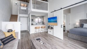 Un vaste espace de vie doté d’un haut plafond, d’un escalier en bois, d’une cuisine avec des tabourets de bar et d’une chambre à coucher avec un grand lit.