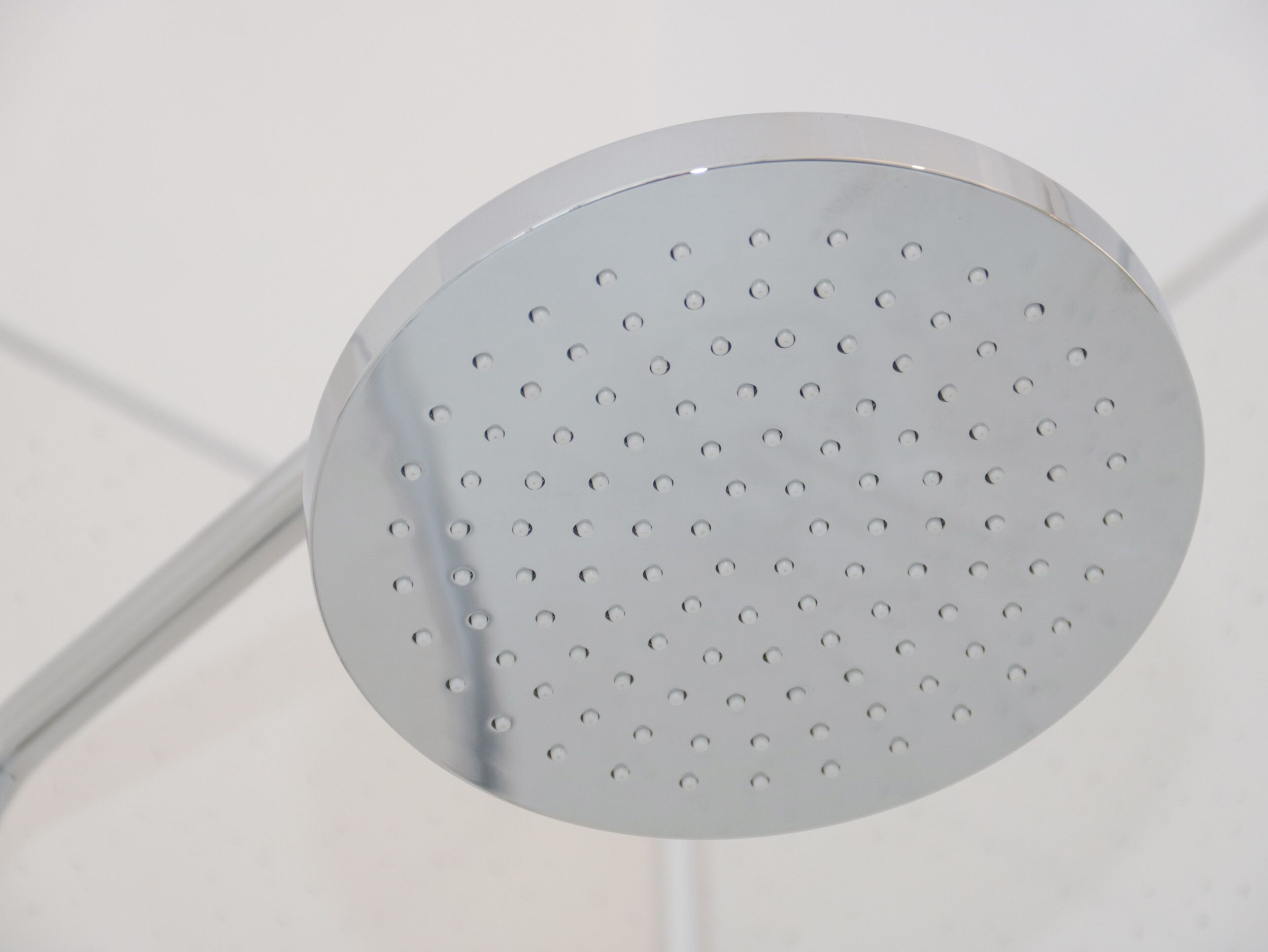Un objeto metálico circular y perforado, probablemente un cabezal de ducha, sujeto a una estructura blanca.