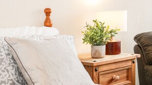 A neatly made bed with patterned bedding, a bedside table with a potted plant, a wooden nightstand, and a lamp. - Gerrard House Apartment (Llandudno)