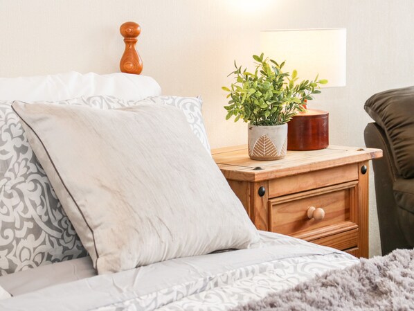 A neatly made bed with patterned bedding, a bedside table with a potted plant, a wooden nightstand, and a lamp.