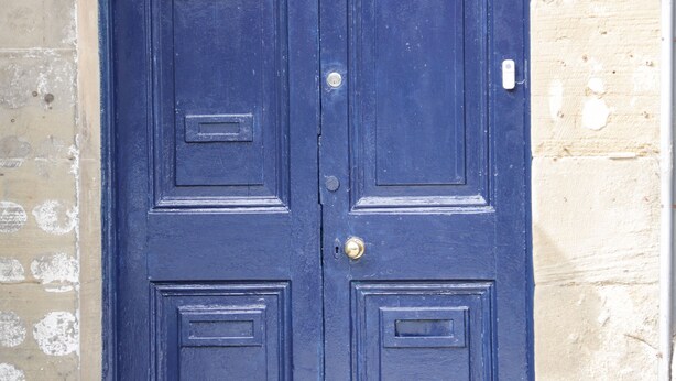 A blue door with two rectangular panels and a brass handle. - Gerrard House Apartment (Llandudno)