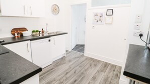 A modern kitchen with white cabinets, a black countertop, and a wooden floor. - Gerrard House Apartment (Llandudno)