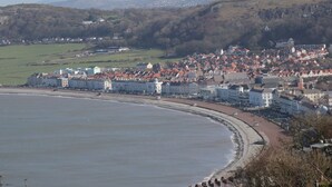A coastal town with a beach, buildings, and hills in the background. - Gerrard House Apartment (Llandudno)