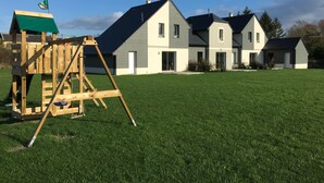 A residential area with a wooden play structure and a row of modern houses with large windows and a well-maintained lawn. - GITE ET SPA LES CABANES 1 à 4 PERS, BAIE DE SOMME (Grand Laviers)