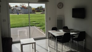 A modern dining area with a table, chairs, and a view of a grassy yard through a sliding glass door. - GITE ET SPA LES CABANES 1 à 4 PERS, BAIE DE SOMME (Grand Laviers)