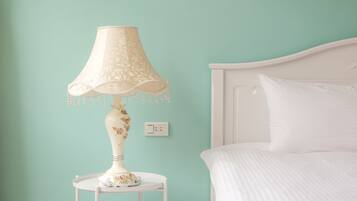 A bed with white bedding, a white nightstand with a lamp, and a light switch on the wall.