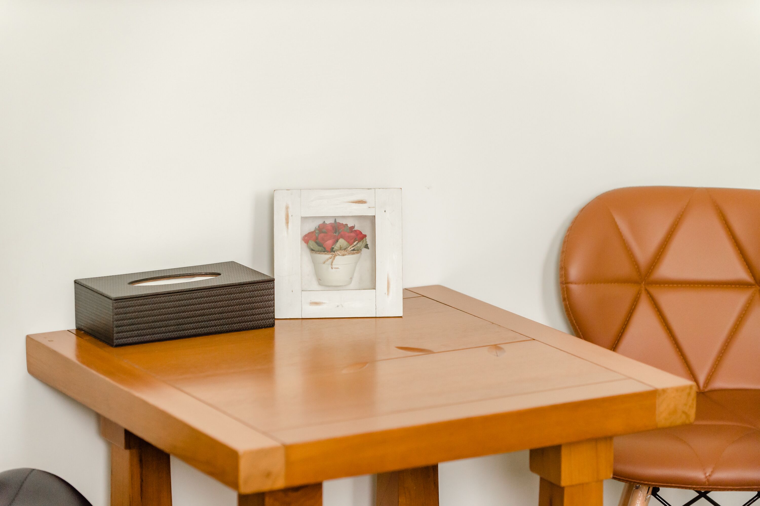 A wooden table with a tissue box and a framed picture of flowers.
