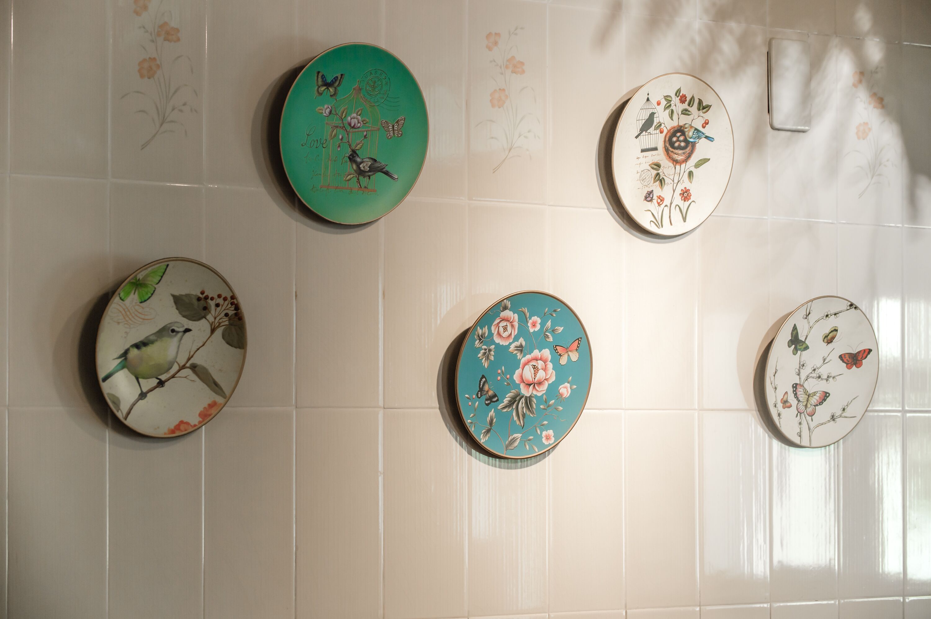 Una pared con cinco platos de cerámica decorados con diseños de pájaros y flores.