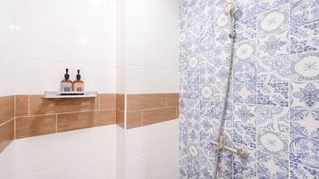 Une salle de bain avec des carreaux blancs et bruns, une douche avec un mur orné d’un motif bleu, et deux bouteilles de shampoing posées sur une étagère.