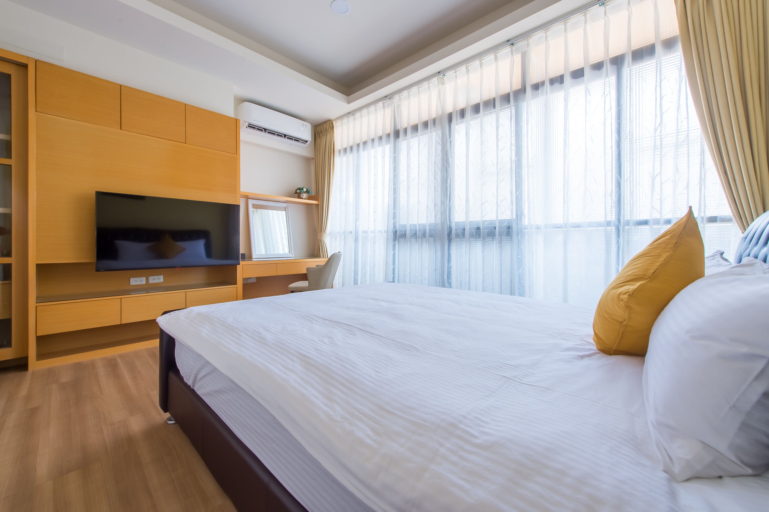 A hotel room with a large bed, a TV, a desk, and a window with curtains.