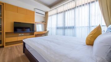 A hotel room with a large bed, a TV, a desk, and a window with curtains.