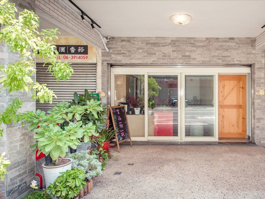 A building entrance with a brick facade, a closed shutter, and a variety of potted plants.