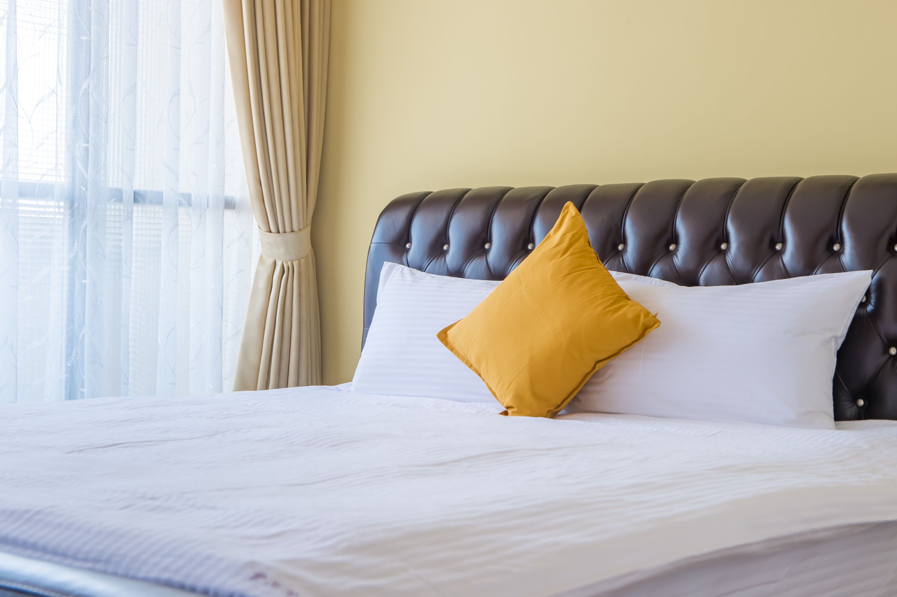 Una cama bien hecha con un cabecero capitonado, una almohada blanca y una almohada color mostaza.