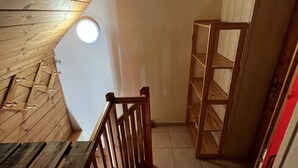 A wooden staircase with a view of the upper floor, a small circular window, and a wooden shelf unit.