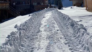 A snow-covered path leading to wooden buildings with balconies, surrounded by a mountainous landscape.