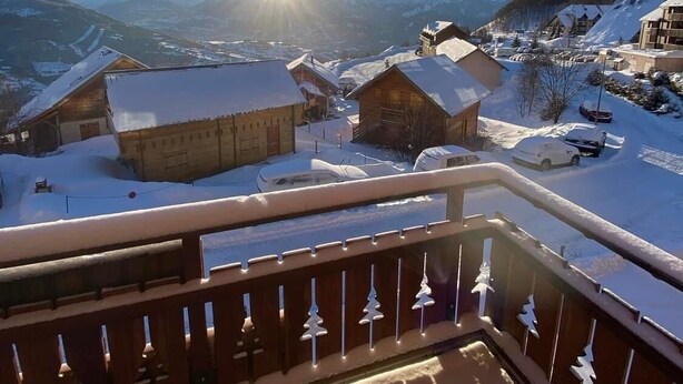 A snow-covered village with traditional wooden houses, a clear sky, and the sun shining.