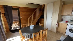 A compact living space with a dining table, wooden chairs, a sofa, a washing machine, and a kitchen area.