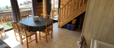 A spacious room with a wooden staircase, a dining table with chairs, and a view of the outdoors.