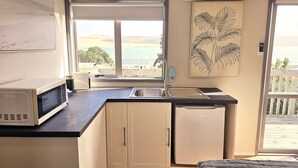 A compact kitchen with a microwave, sink, and refrigerator, featuring a large window with a view of the sea. - Cosy Opononi cabin with gorgeous ocean views - relaxation bliss!  (Opononi)