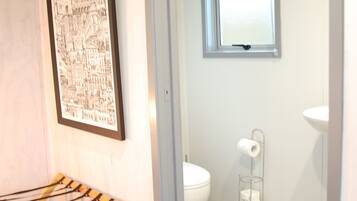 Ein Badezimmer mit Toilette, Fenster, Waschbecken und einem Stadtbild als Bild an der Wand.
