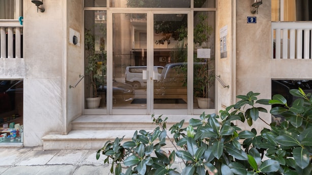A building entrance with a glass door, potted plants, and a number sign. - Bang in Kolonaki by Athenian Homes (Athens)