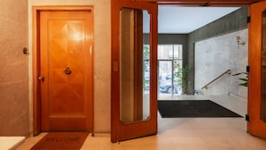A hotel entrance with a wooden door, a welcome mat, and a view of the outside through a glass door. - Bang in Kolonaki by Athenian Homes (Athens)