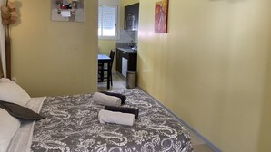Un dormitorio con cama, almohadas, una mesita de noche, un televisor de pared y una ventana con persianas.