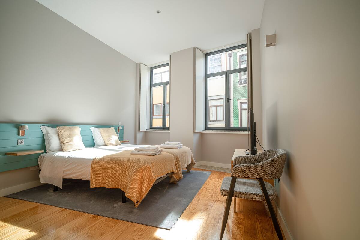 A bedroom with a bed, two bedside tables, a chair, and large windows.