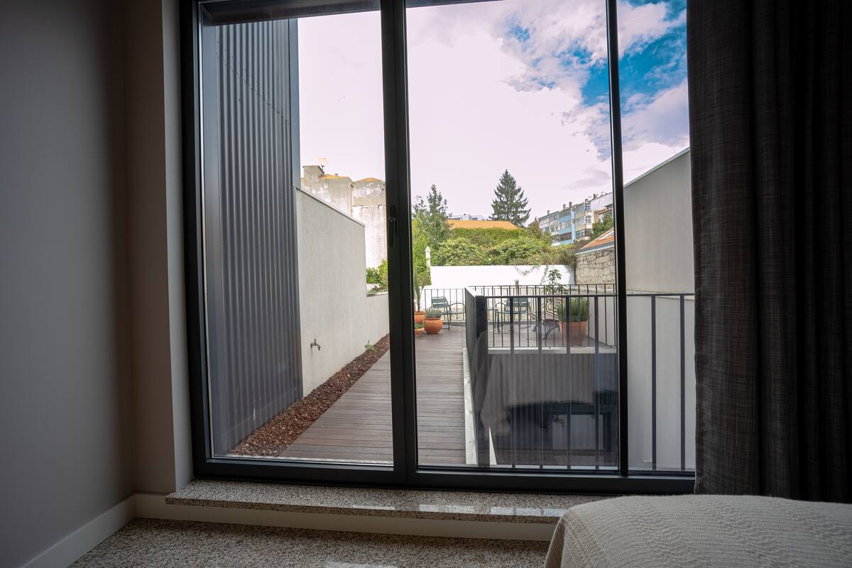 A room with a large sliding glass door leading to a balcony with a view of a cityscape and greenery.