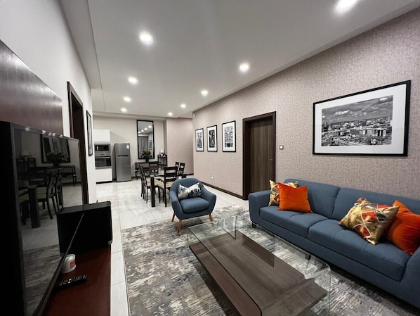 A modern living room with a blue sofa, a coffee table, and a dining area with chairs and a table.