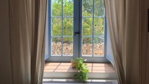 A window with beige curtains, a view of greenery outside, and a small plant on the windowsill. - Masseria Santacatrini - Loft Nocellara (Melilli)