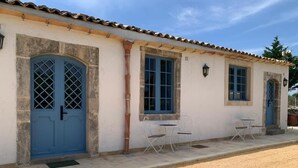 A building with a tiled roof, two blue doors, and a small outdoor seating area with two tables and four chairs. - Masseria Santacatrini - Loft Nocellara (Melilli)