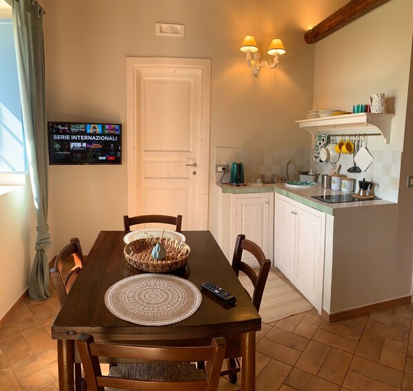 A dining area with a TV displaying a series menu, a wooden table with chairs, a woven basket, and a remote control.