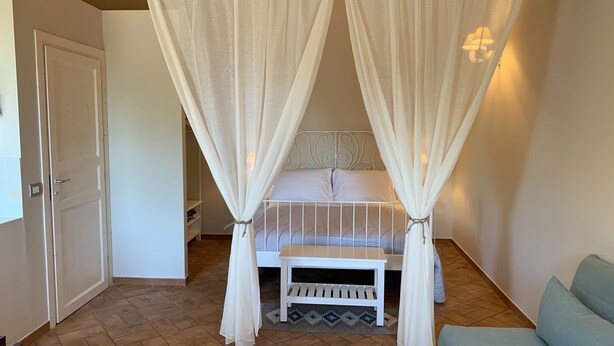 Un dormitorio con cama con dosel, una mesita de noche, una silla y una puerta.