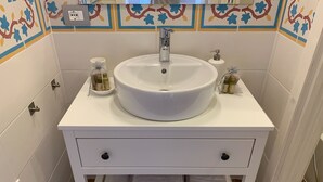 Un baño con un lavamanos blanco, dos botellas de jabón para manos y un toallero con toallas dobladas.