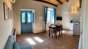 Amplia sala de estar con una mesa de comedor, una cocina y una puerta azul que da al exterior.