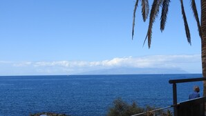 Une vue sur la côte, avec un ciel dégagé, une rive rocheuse et une personne debout sur un balcon.